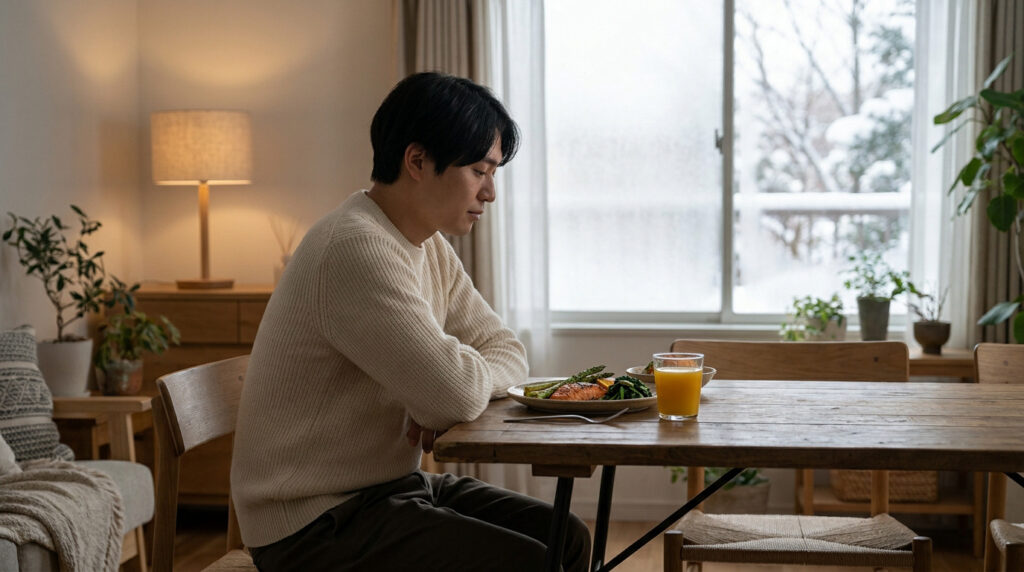 Un homme assis à une table en bois mangeant un repas sain près d'une fenêtre avec de la neige à l'extérieur.