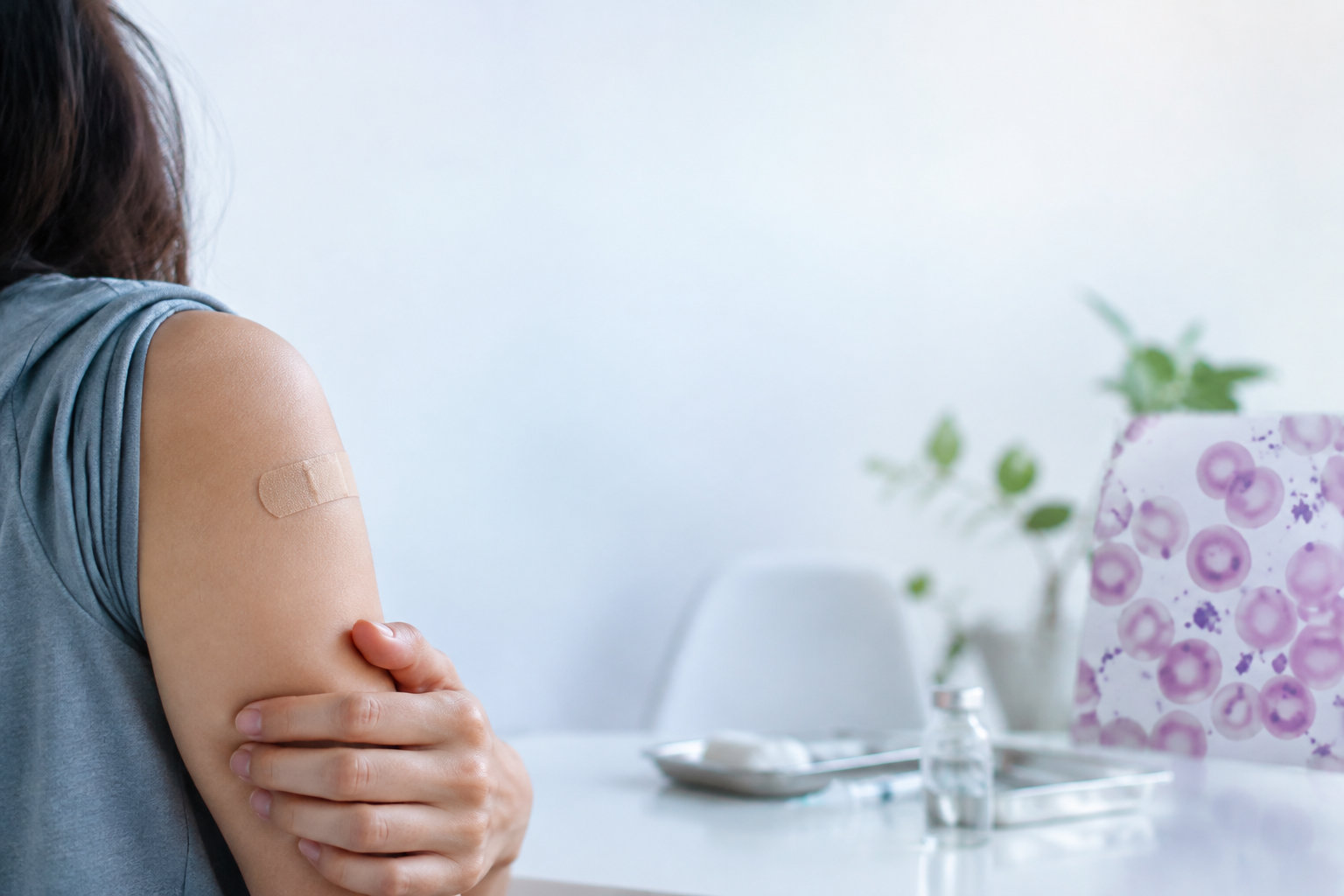 Une personne montre le pansement sur son bras après une vaccination, avec un frottis sanguin en arrière-plan.